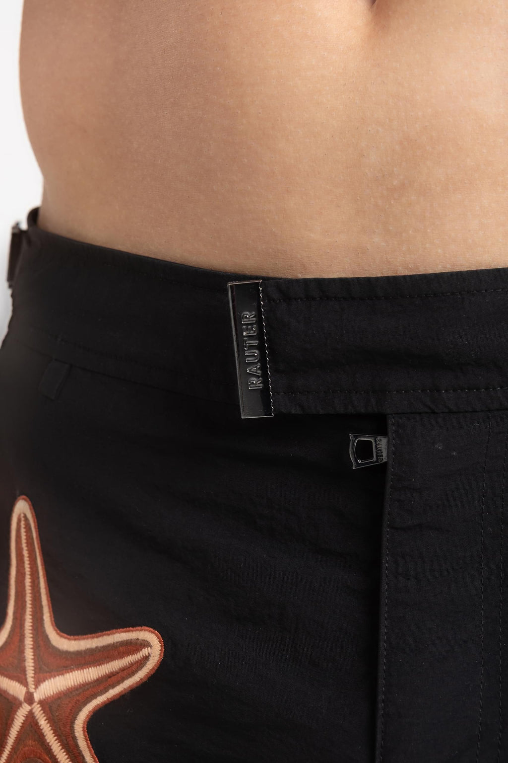 Homem usando short de praia RAUTER TRÊS ESTRELAS MÉDIO, com bordado industrial de estrelas-do-mar sobre nylon reciclado e estilo sofisticado.