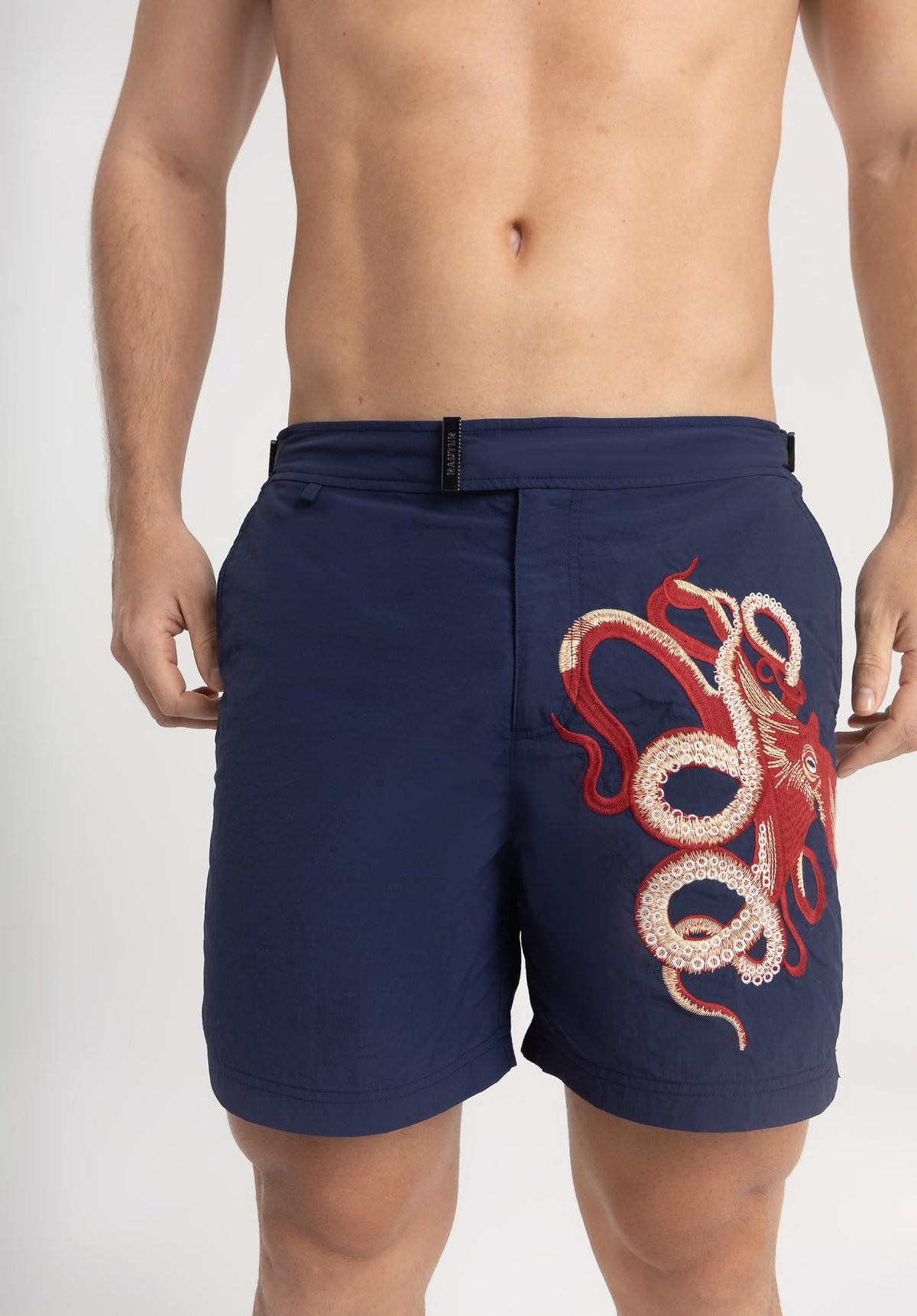 Homem usando short de praia RAUTER POLVO MÉDIO, com bordado industrial de polvo sobre nylon reciclado e estilo sofisticado.