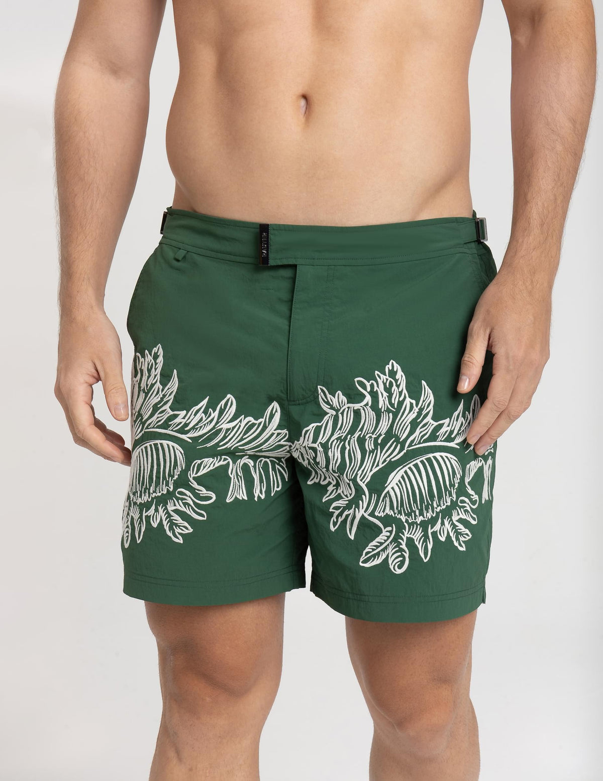 Homem usando short de praia RAUTER CORAIS MÉDIOS, com bordado industrial de corais sobre nylon reciclado e estilo sofisticado.